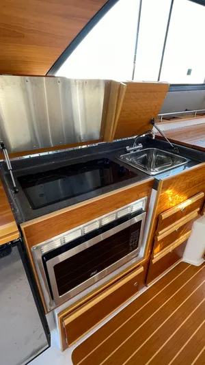  Yacht Photos Pics 2022 Cutwater C-32 Sedan kitchen with stove, sink, and wooden cabinetry.
