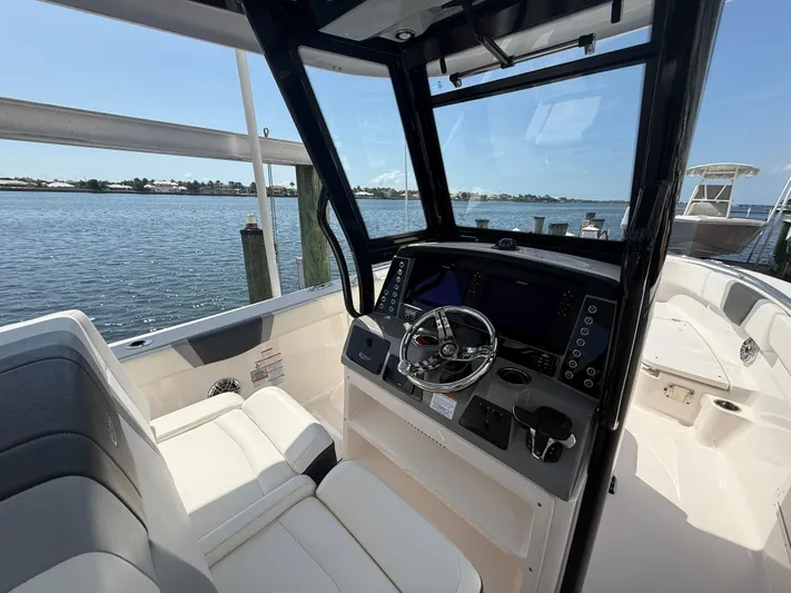 272-203 Brokerage Sebastian Yacht Photos Pics 2023 Robalo R272 Center Console boat interior with steering wheel and seating, docked by the water.