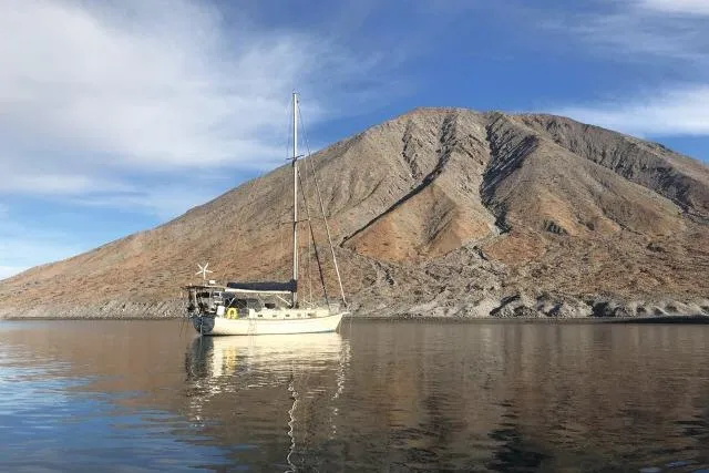 Wild Blue Yacht Photos Pics Sailboat Island Packet 45 (1999) anchored near a rocky mountain under a blue sky.