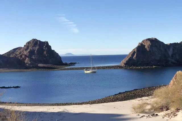 Wild Blue Yacht Photos Pics Sailboat anchored in a serene bay, surrounded by rocky cliffs and clear blue water.