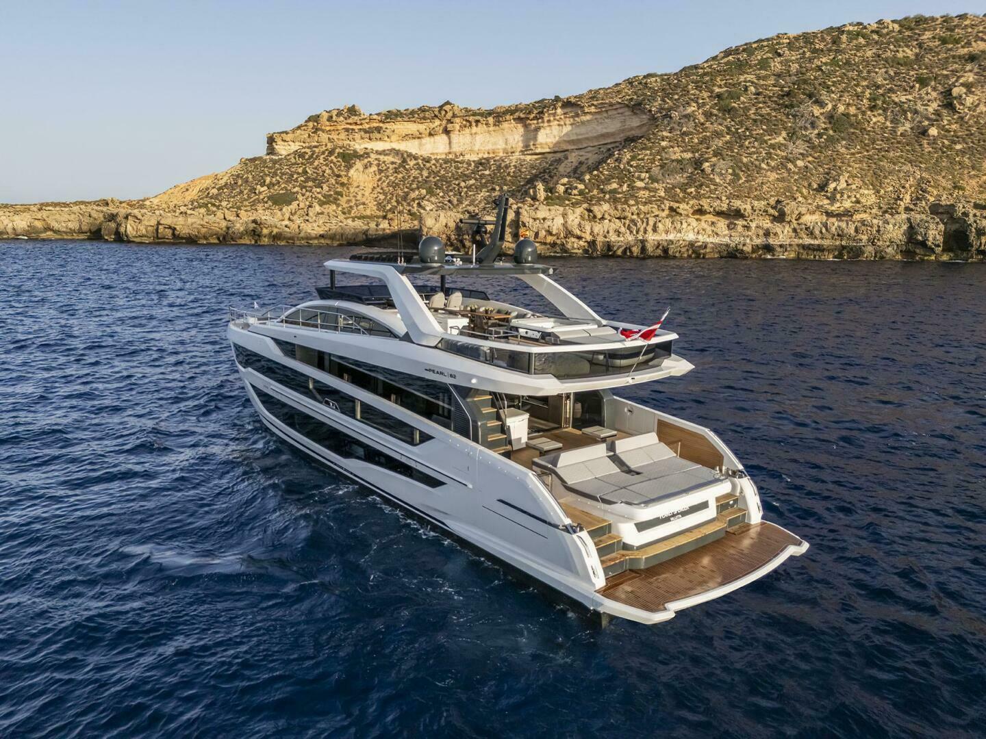 Luxurious 2026 Pearl 82 yacht cruising near rocky coastline in clear blue waters.