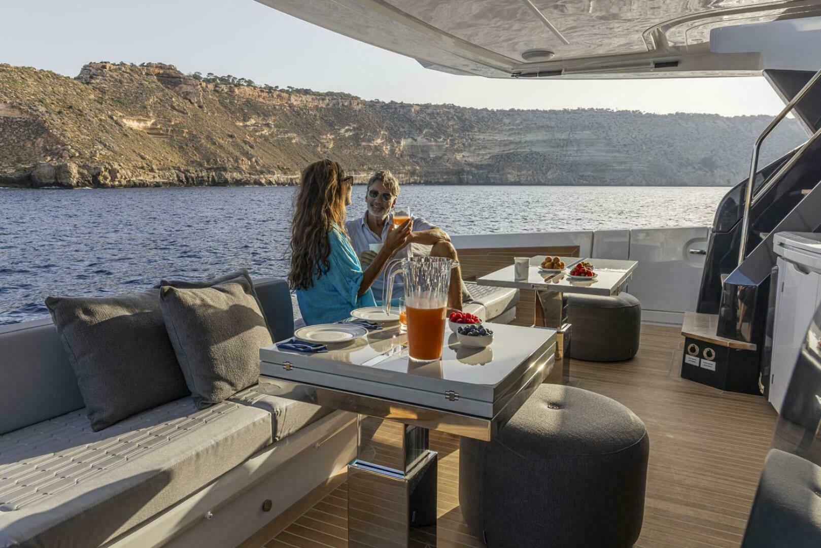 Couple enjoying drinks on a luxurious 2026 Pearl 82 yacht with scenic ocean view.