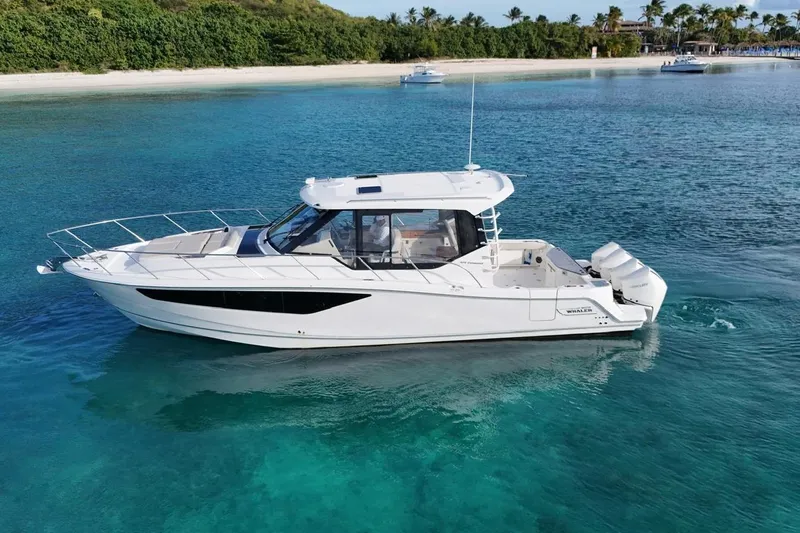  Yacht Photos Pics 2022 Boston Whaler 405 Conquest cruising in clear blue waters near a tropical shoreline.
