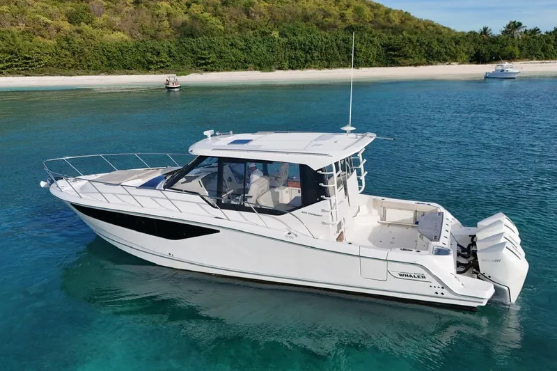  Yacht Photos Pics 2022 Boston Whaler 405 Conquest boat on clear blue water near a sandy beach.