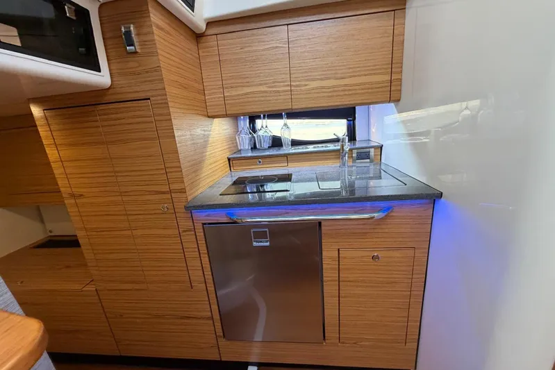  Yacht Photos Pics Modern kitchen area in 2022 Boston Whaler 405 Conquest boat, featuring wood cabinetry and stainless steel appliances.