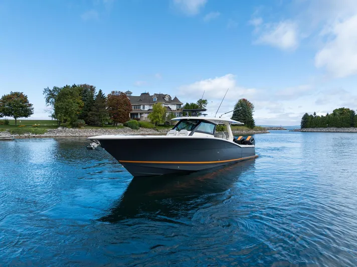  Yacht Photos Pics 2023 Scout 425 LXF boat cruising on a serene lake near a picturesque shoreline.