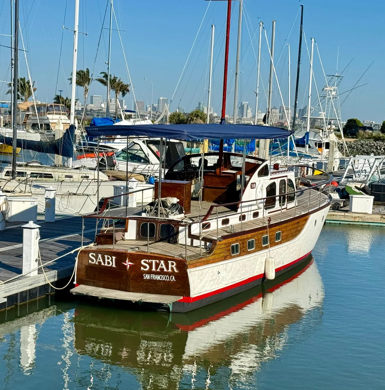 Classic 1966 Rampart 48 yacht docked in a marina, featuring wooden details and a blue canopy.
