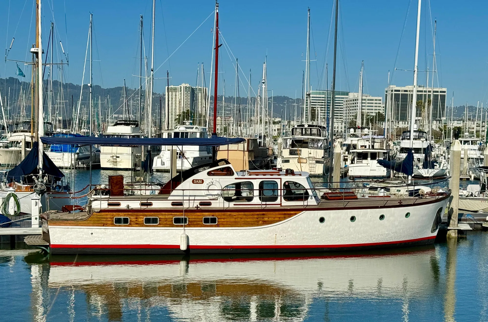 1966 Rampart 48 yacht docked in a marina, surrounded by sailboats and cityscape.