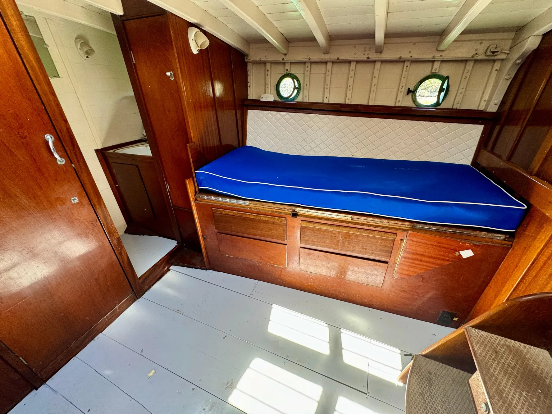 1966 Rampart 48 yacht interior with wooden paneling, blue cushioned bed, and porthole windows.