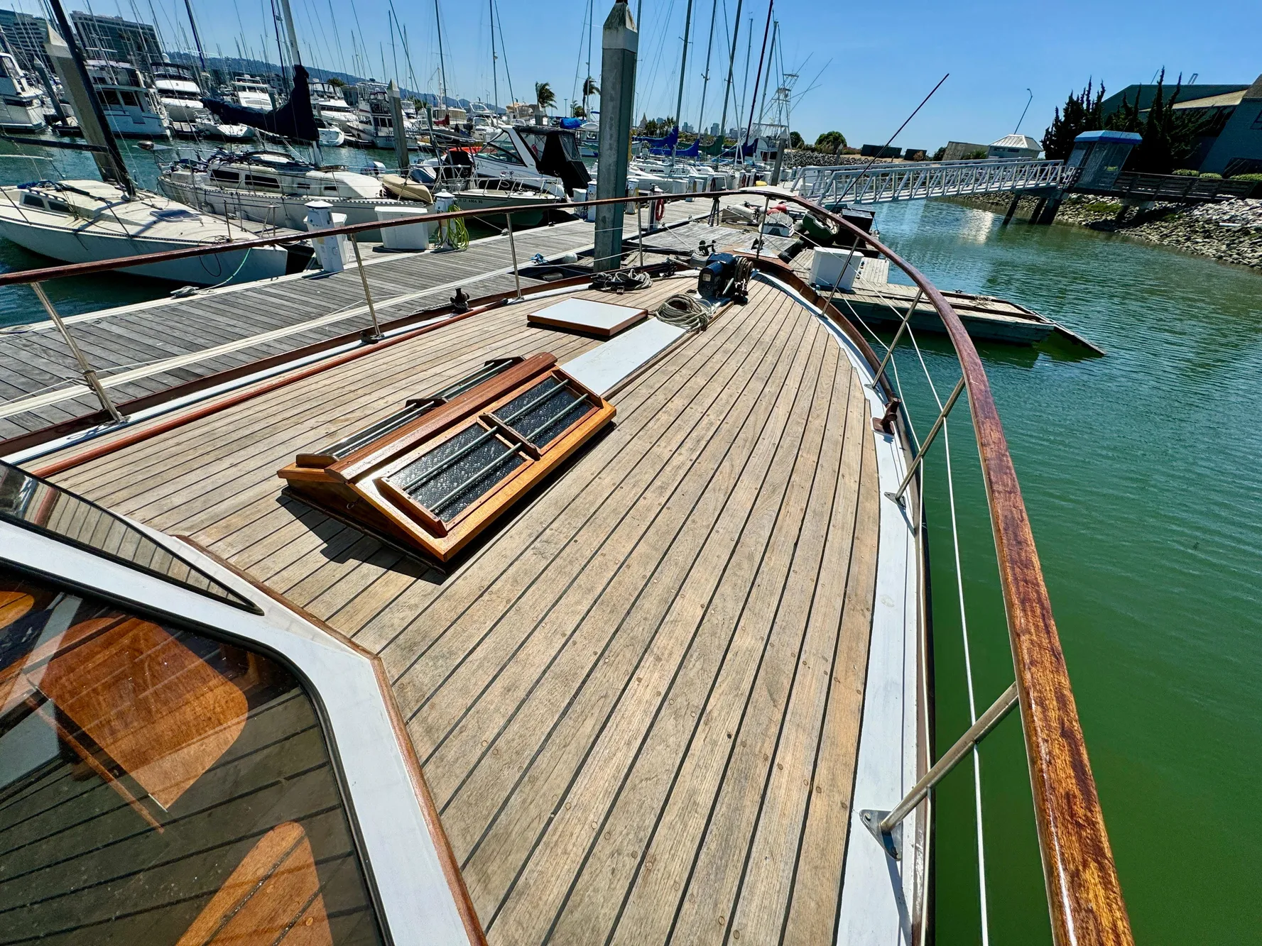1966 Rampart 48 yacht with wooden deck, docked in a marina under clear skies.