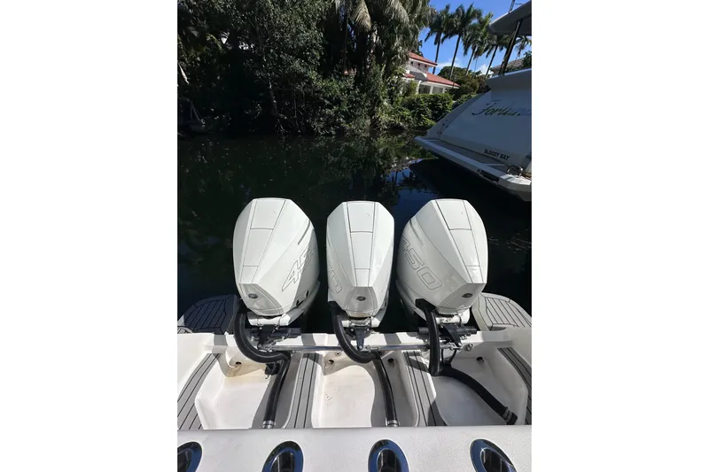 No Name Yacht Photos Pics Triple outboard engines on a 2020 Intrepid 409 Valor boat, docked near lush greenery.