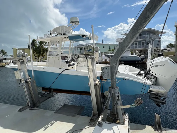  Yacht Photos Pics Blue and white Young 27 boat on lift, dockside, under a partly cloudy sky.