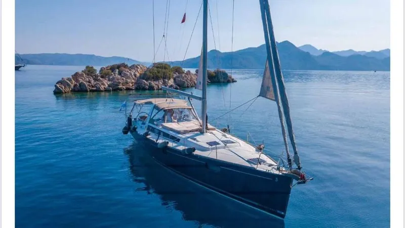  Yacht Photos Pics 2014 Beneteau Oceanis 48 sailing near rocky island, calm blue waters, and distant mountains.