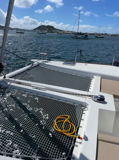 Pasha Yacht Photos Pics Lagoon 450F catamaran deck with netting, ocean view, and moored boats in the background.