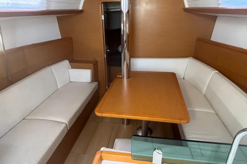 Eclipse Yacht Photos Pics Interior of 2018 Jeanneau Sun Odyssey 389 sailboat with wooden table and white seating.