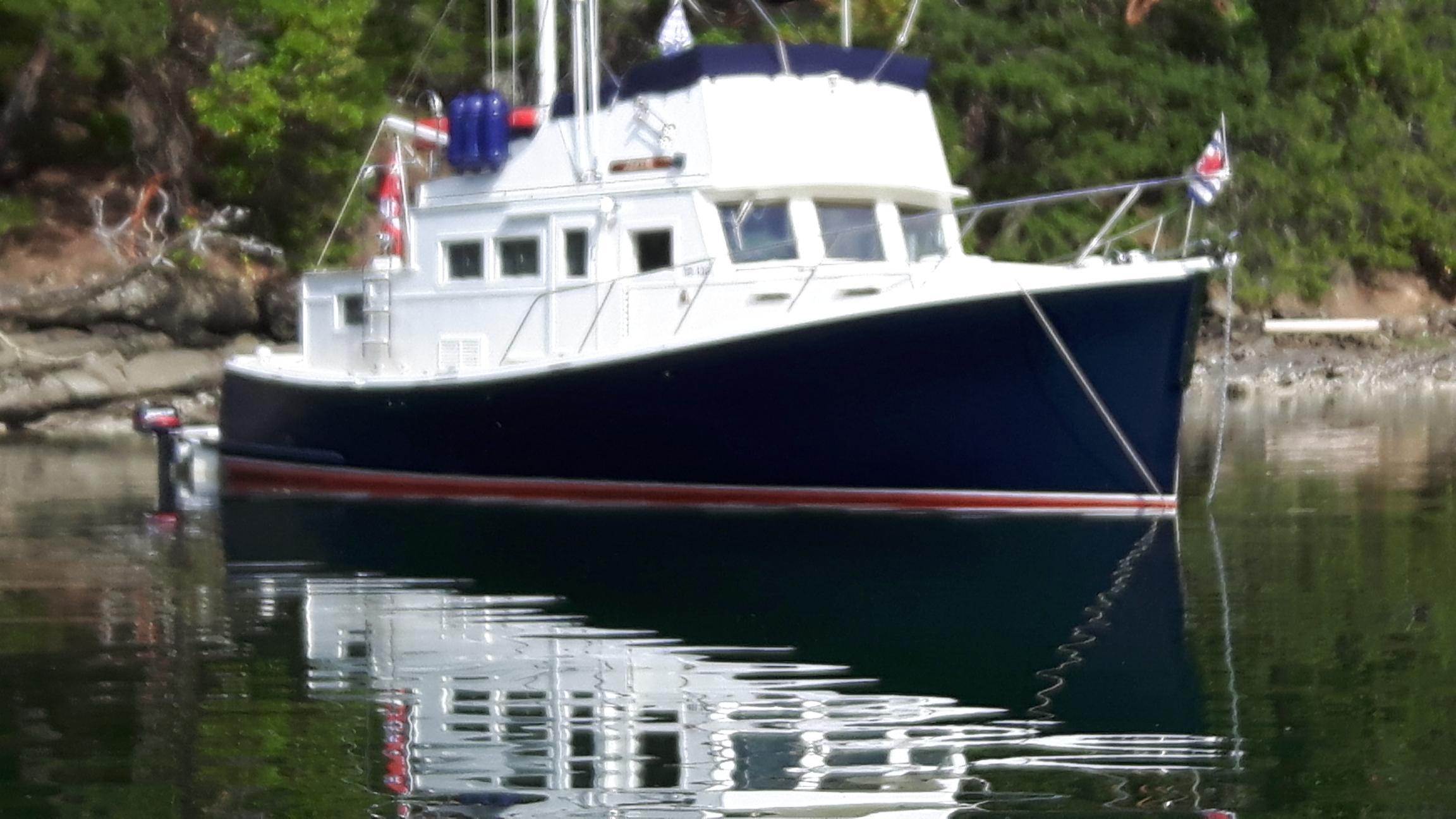 1970 Custom Tri-Cabin boat on calm water, surrounded by lush greenery.