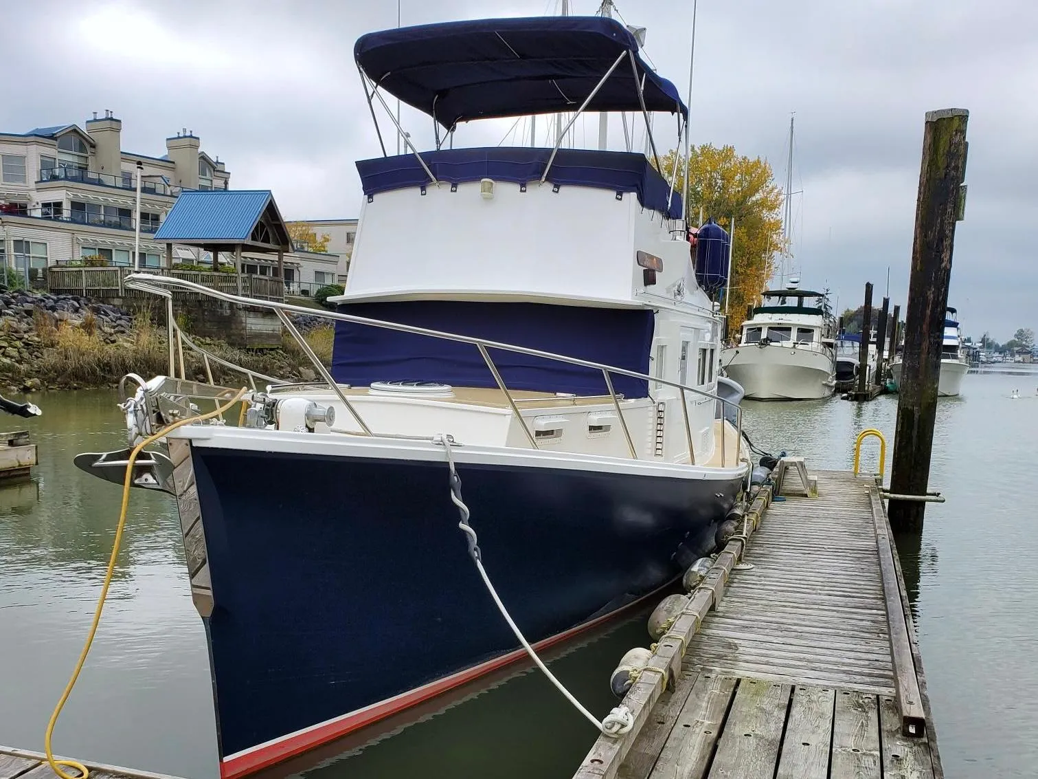 1970 Custom Tri-Cabin boat docked at marina, overcast sky, waterfront buildings in background.