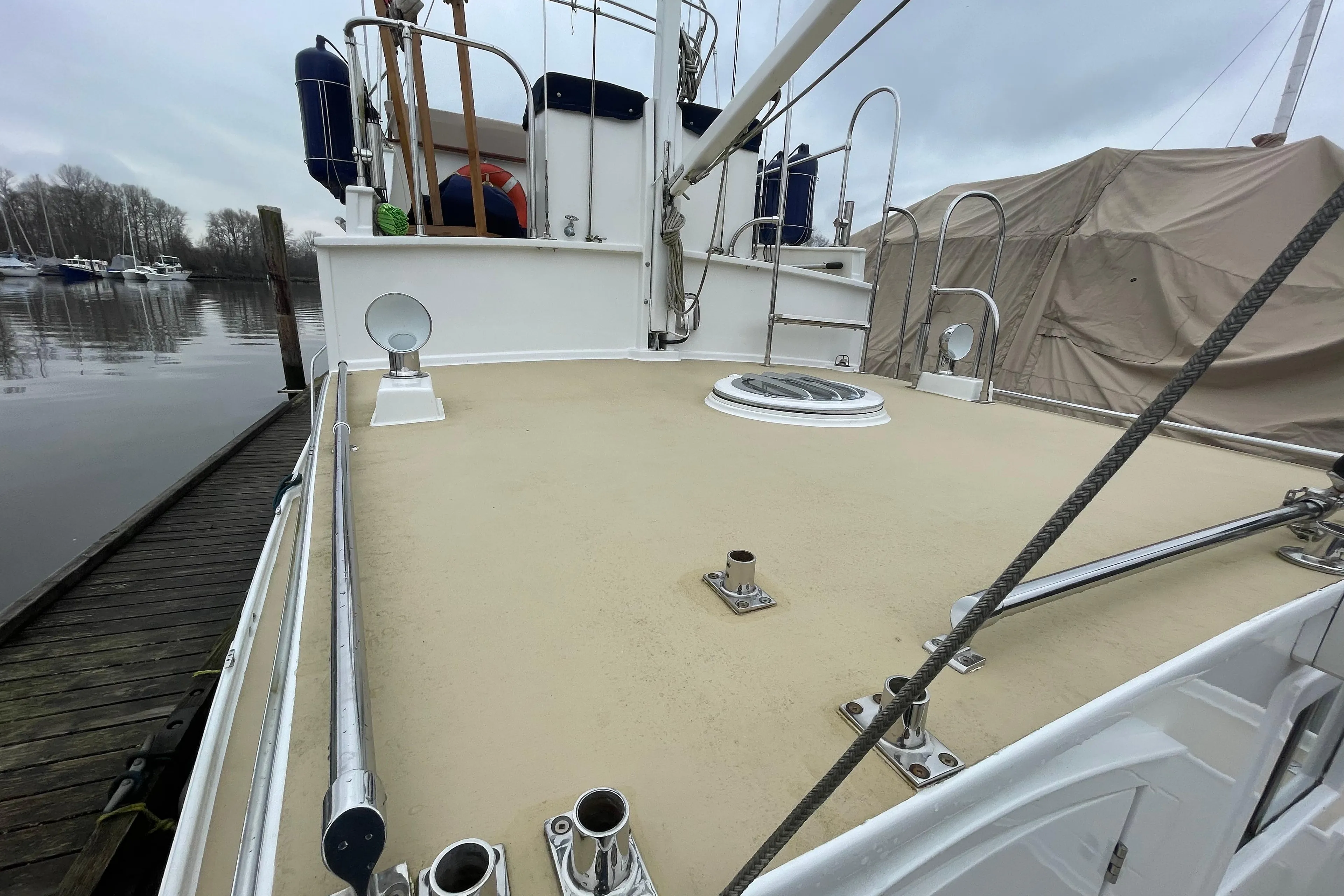 1970 Custom Tri-Cabin boat deck with railing, docked at marina under cloudy sky.