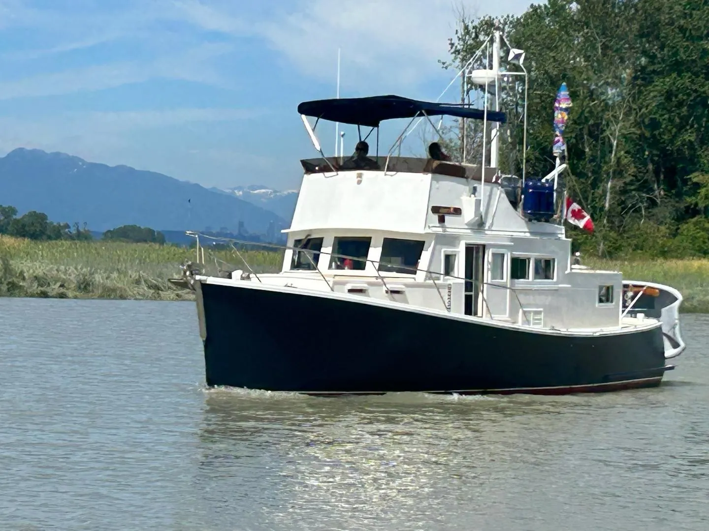 1970 Custom Tri-Cabin boat cruising on a scenic river with mountains in the background.