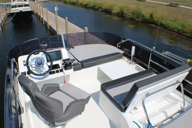  Yacht Photos Pics 2020 Jeanneau NC 1095 Flybridge with modern helm and seating, docked by a serene waterway.