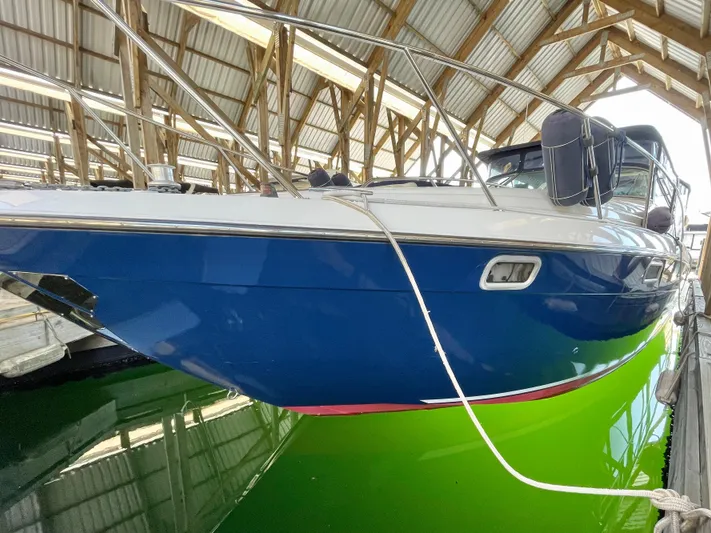 Hailey Brae Yacht Photos Pics 2021 Custom Express Cruiser in dock, blue hull, under wooden canopy.