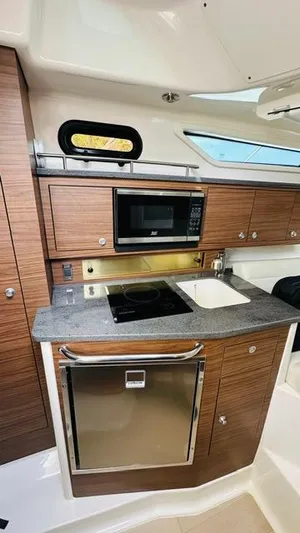  Yacht Photos Pics 2023 Boston Whaler 325 boat kitchen with wood cabinets, microwave, sink, and stove.