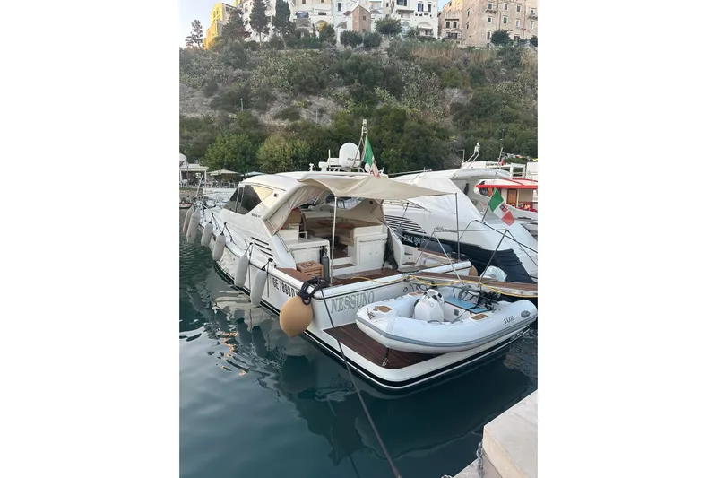  Yacht Photos Pics 2005 Uniesse 48 Open yacht docked with inflatable boat, scenic backdrop.