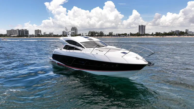 Arbitrage Yacht Photos Pics 2017 Sunseeker Predator 57 yacht cruising near a city shoreline under a blue sky.