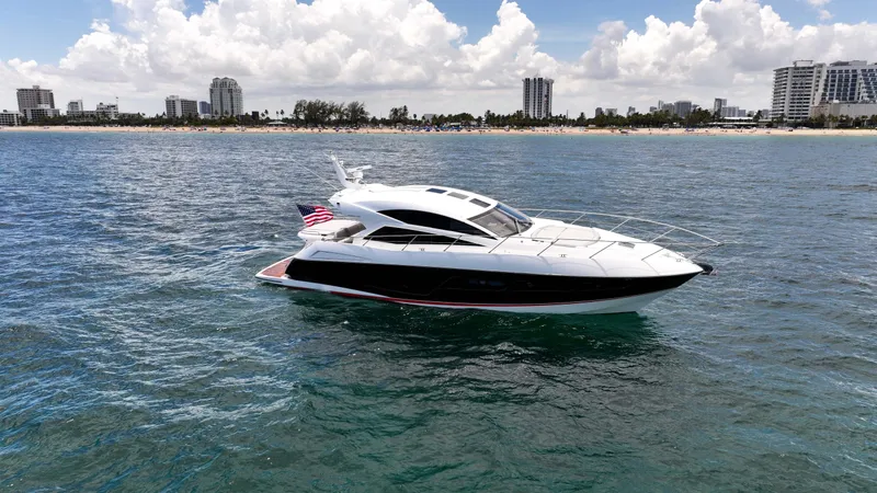 Arbitrage Yacht Photos Pics 2017 Sunseeker Predator 57 yacht cruising near a city shoreline under a cloudy sky.