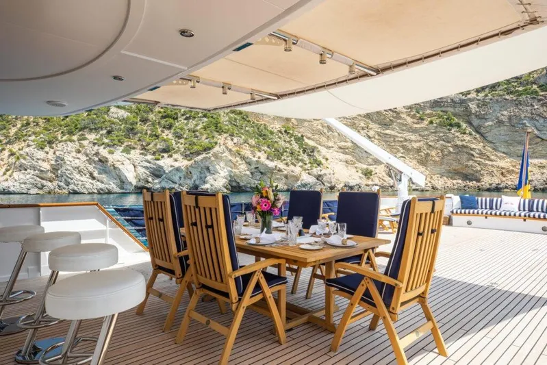  Yacht Photos Pics Luxurious dining setup on 1982 Feadship Classic yacht with scenic coastal backdrop.