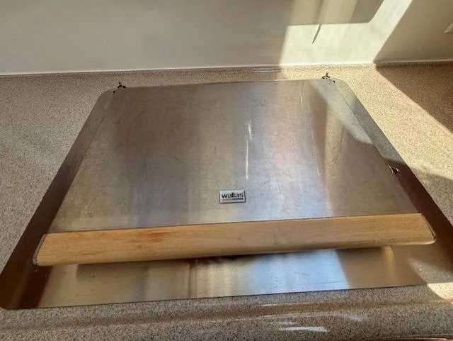 Island Dreamer Yacht Photos Pics Stainless steel cover with wooden handle on a countertop, reflecting sunlight.