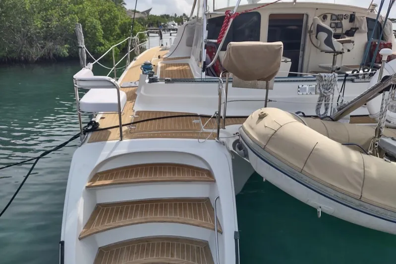 Nyango Yacht Photos Pics 1996 Fountaine Pajot Venezia 42 catamaran with wooden deck and inflatable dinghy, docked in calm waters.