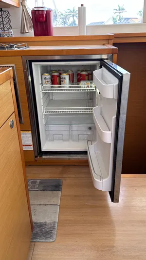 Aquamarine Yacht Photos Pics Open mini fridge in Lagoon 450 F yacht kitchen, stocked with cans, wooden cabinetry.