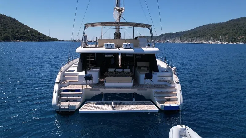 Welcome Back Yacht Photos Pics Luxurious 2019 Sunreef 50 catamaran anchored in serene blue waters, surrounded by lush hills.