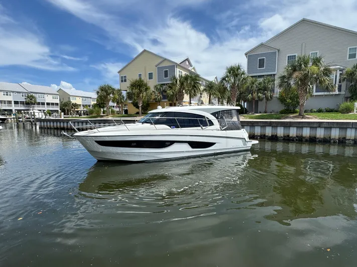  Yacht Photos Pics 2024 Beneteau Antares 11 boat on calm water near waterfront homes.