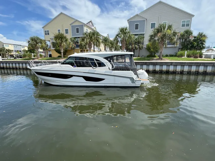  Yacht Photos Pics 2024 Beneteau Antares 11 boat docked near waterfront homes, under a clear sky.