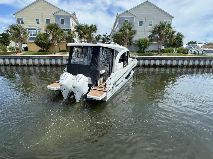  Yacht Photos Pics 2024 Beneteau Antares 11 boat cruising in a canal near waterfront homes.