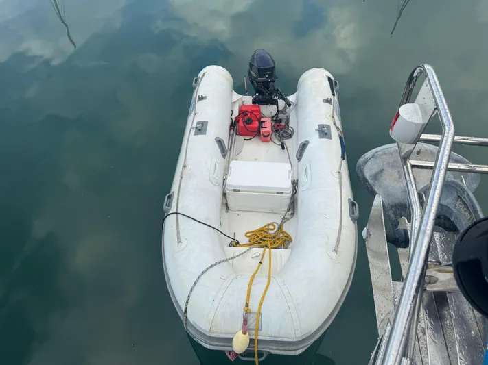 Liquid Sunshine Yacht Photos Pics Inflatable dinghy tied to a Beneteau 523 Oceanis, 2005 model, floating on calm water.