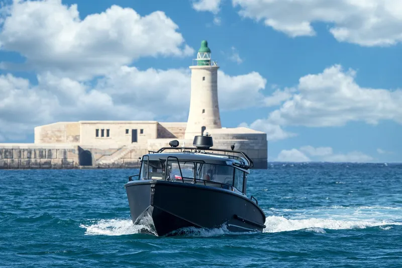  Yacht Photos Pics 2026 XO Boats EXPLR 10S PLUS navigating near a historic lighthouse under a blue sky.