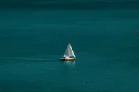 A solitary sailboat on vast, calm turquoise sea under a cloudy sky.