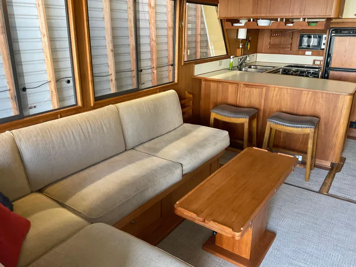  Yacht Photos Pics Cozy 1991 Nordic Pilothouse interior with beige sofa, wooden table, and compact kitchen area.
