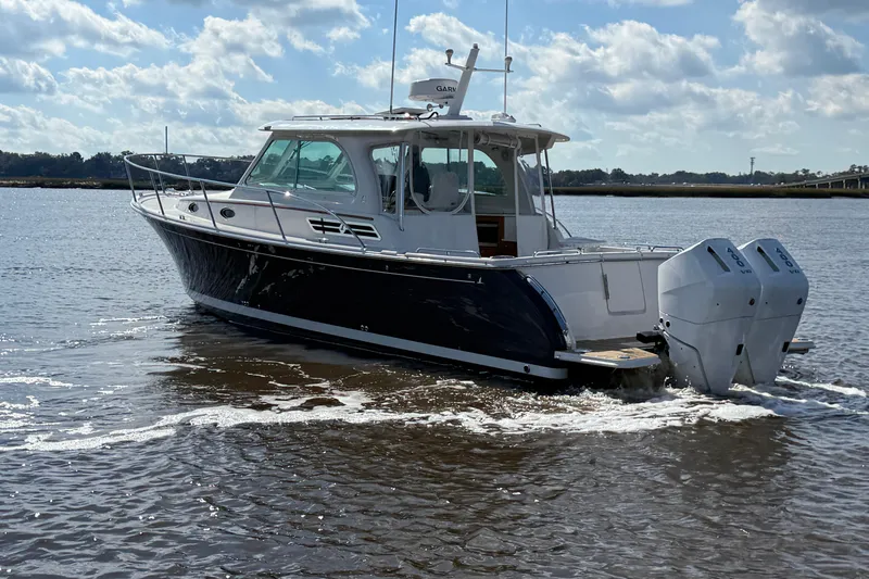  Yacht Photos Pics 2024 Back Cove 34O boat cruising on a calm waterway under a partly cloudy sky.