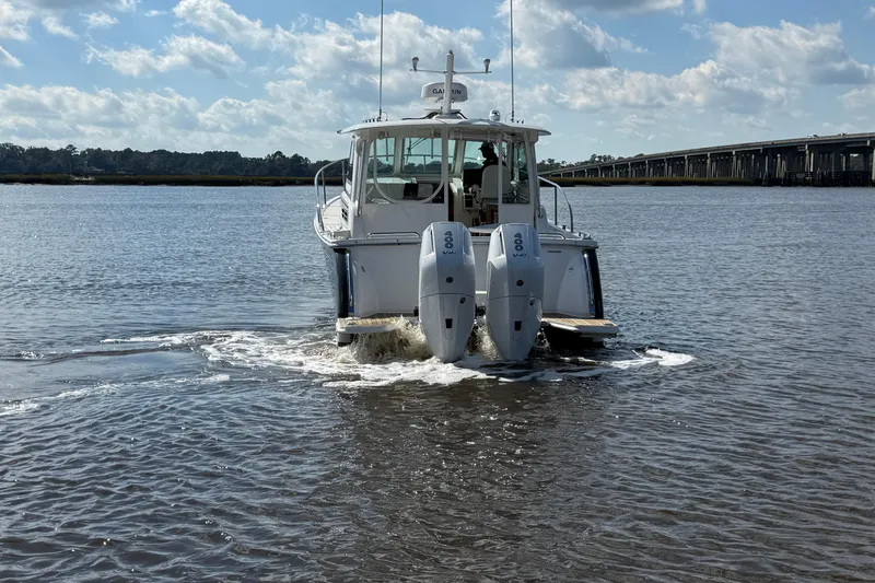  Yacht Photos Pics 2024 Back Cove 34O boat cruising on a calm river under a partly cloudy sky.