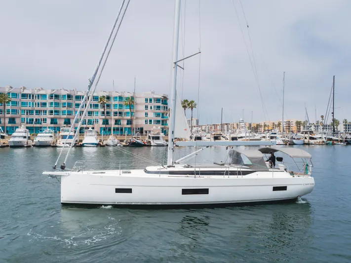 Kalesma Yacht Photos Pics 2021 Bavaria C50 Style yacht sailing in a marina with modern buildings in the background.