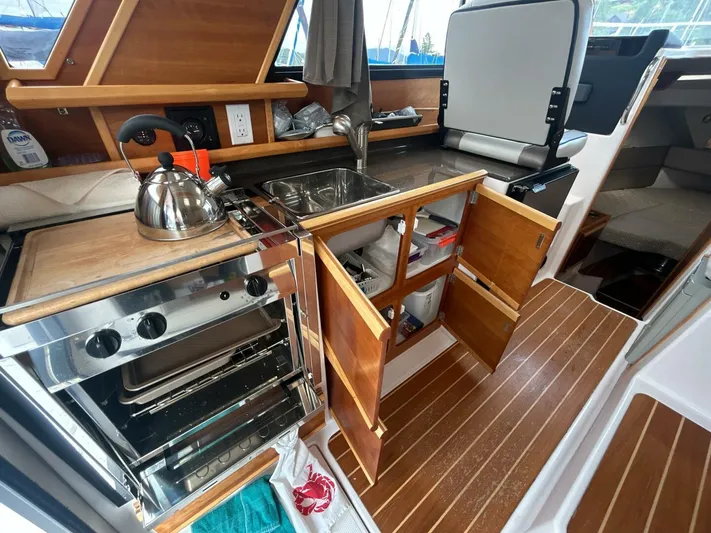  Yacht Photos Pics 2019 Cutwater C-28 boat kitchen with stove, sink, and wooden cabinetry.