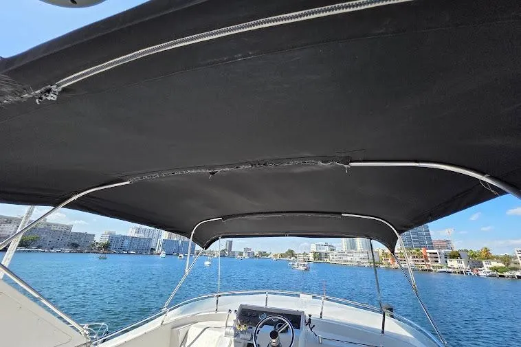  Yacht Photos Pics 1993 McKinna 48 Pilothouse boat with black canopy, overlooking a scenic waterfront cityscape.