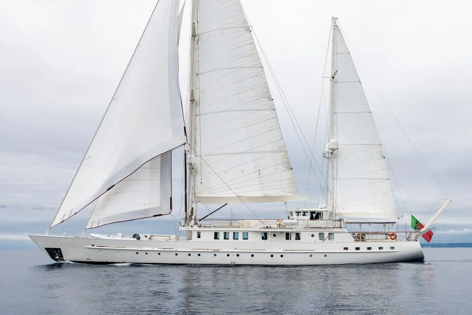 Custom 1990 sailing yacht with white sails on calm sea.