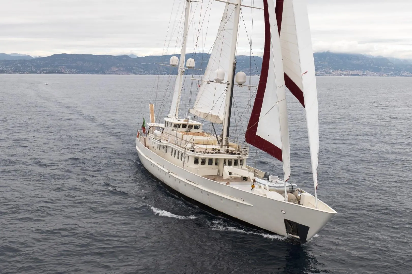 Sailing yacht on open sea, custom model from 1990, with mountains in the background.