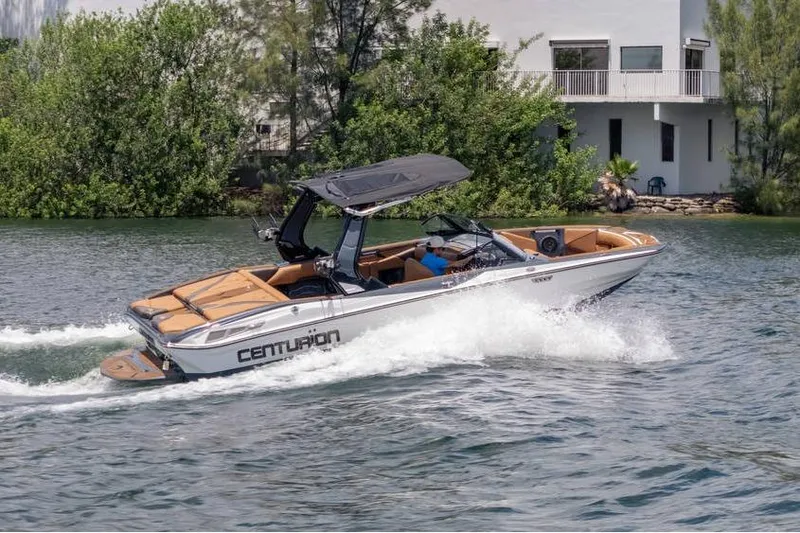  Yacht Photos Pics 2025 Centurion Nv233 boat cruising on a lake near a modern house.