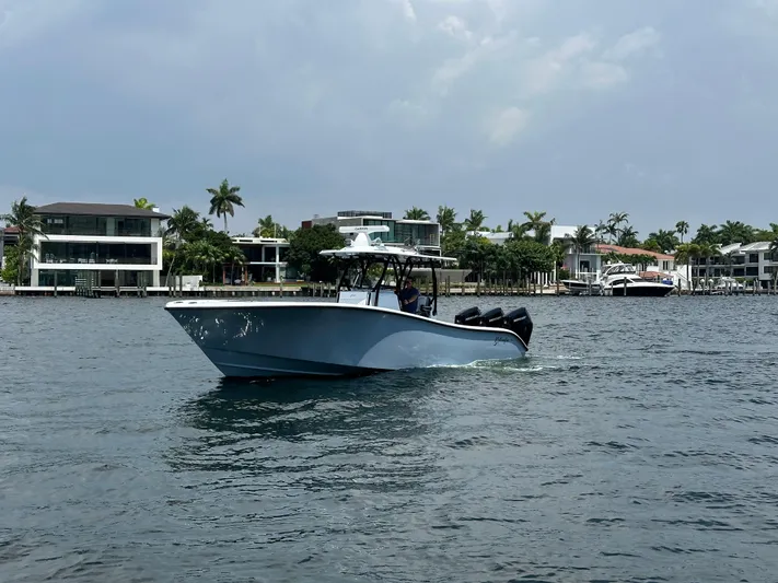  Yacht Photos Pics 2024 Yellowfin 34 Offshore boat cruising near waterfront homes under a cloudy sky.